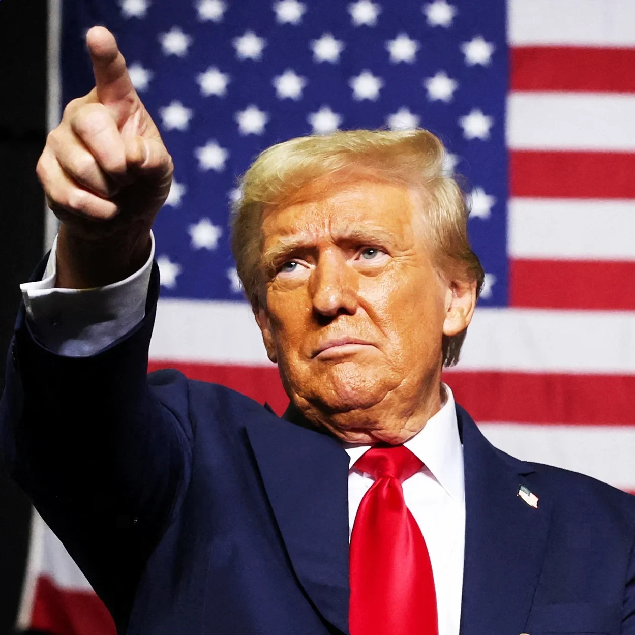 Donald Trump points upward before an American flag
